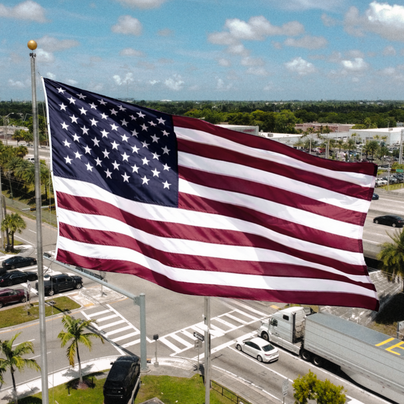 American flag waving in front of a highway with cars and trucks passing by